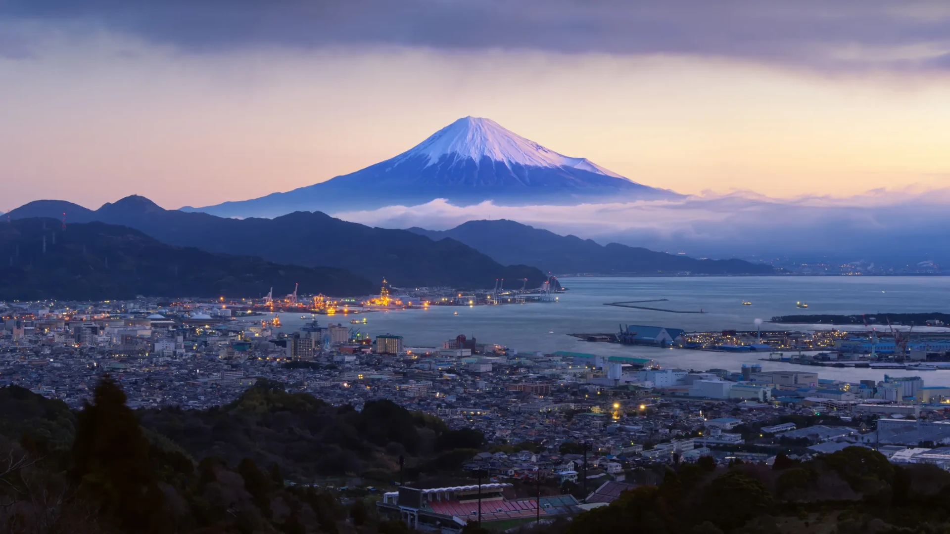 Mount Fuji at dusk above a lit Japanese port city